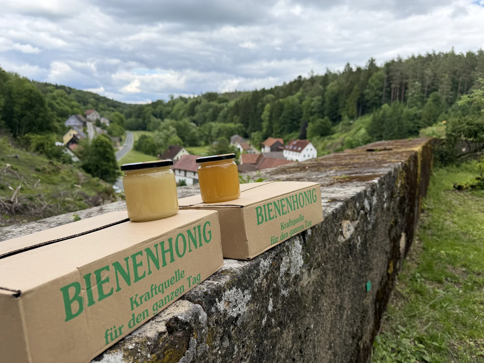 Two jars of Schloss Wiesentfels honey on a stone wall overlooking the valley
