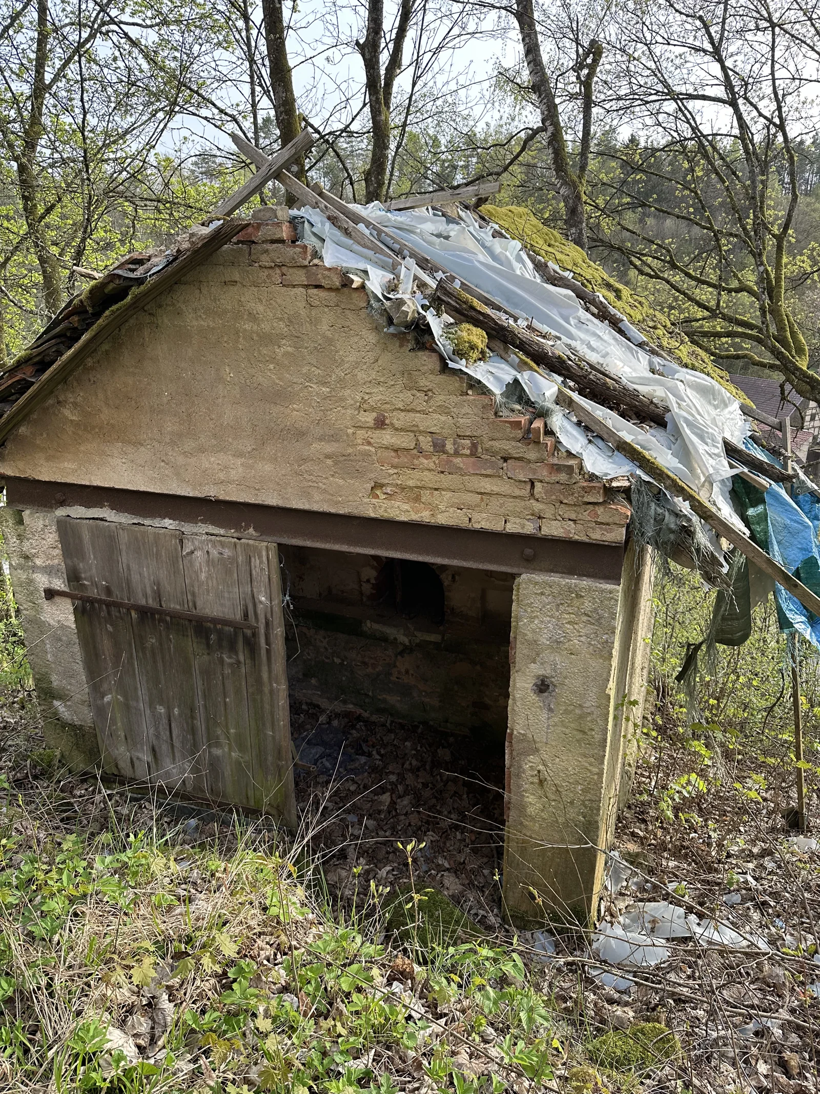 Das separate Backhaus mit offener Holztür und beschädigtem Dach – Archivaufnahme 2024